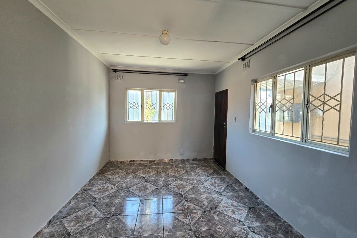 An empty living room featuring tiled flooring, security bars on the windows, and neutral wall finishes, offering a blank canvas for interior design.