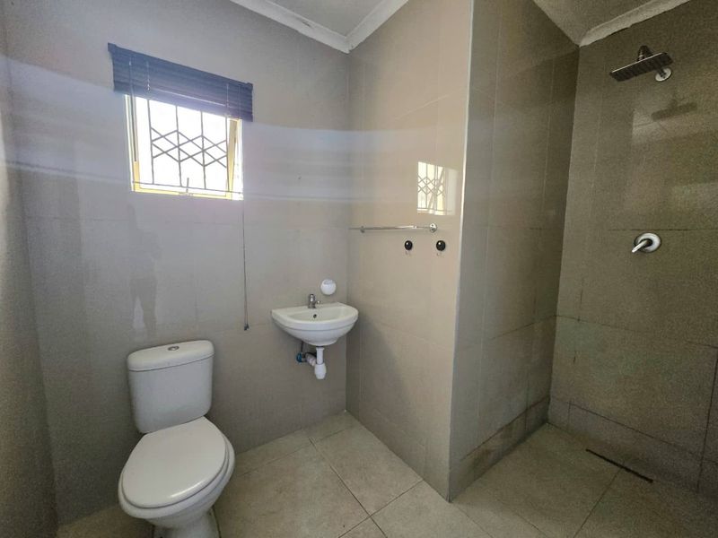 A functional bathroom featuring tiled walls and flooring, a wall-mounted basin, a toilet, and a shower area with a fixed shower head.