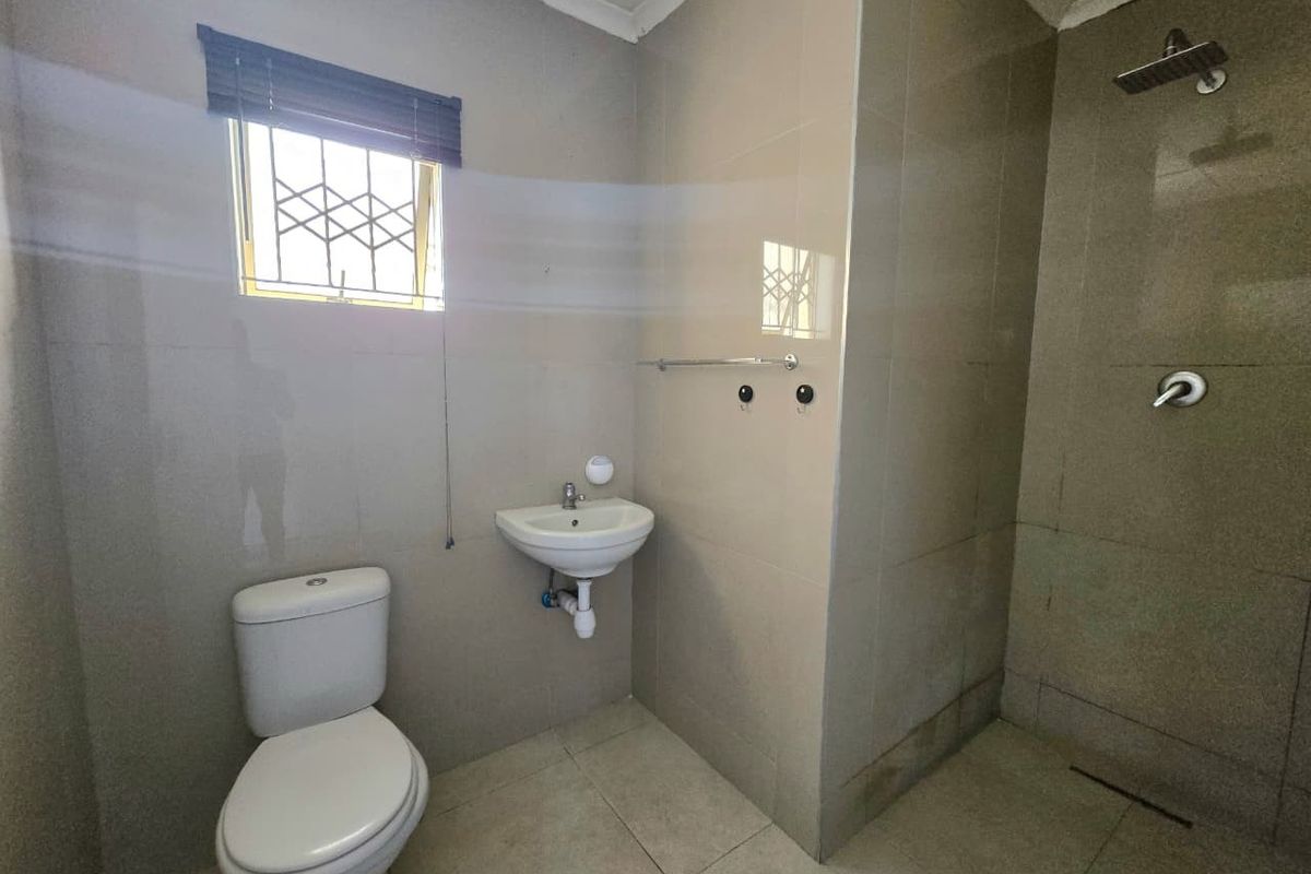 A functional bathroom featuring tiled walls and flooring, a wall-mounted basin, a toilet, and a shower area with a fixed shower head.