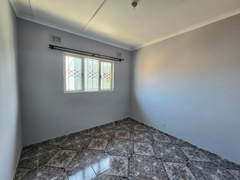 An empty bedroom featuring tiled flooring, neutral wall paint, and a window fitted with security bars.