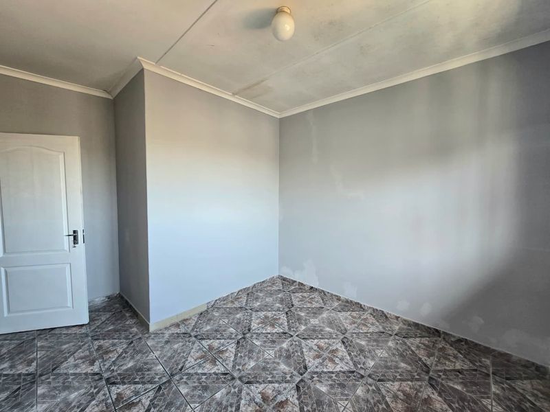 An empty bedroom featuring tiled flooring and neutral walls, requiring minor cosmetic repairs and fresh paint to restore its appeal.