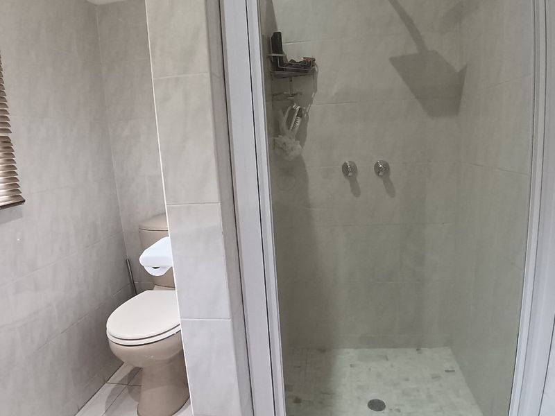 A functional bathroom featuring a glass-enclosed shower with a rain shower head and a separate toilet area with neutral wall and floor tiling.