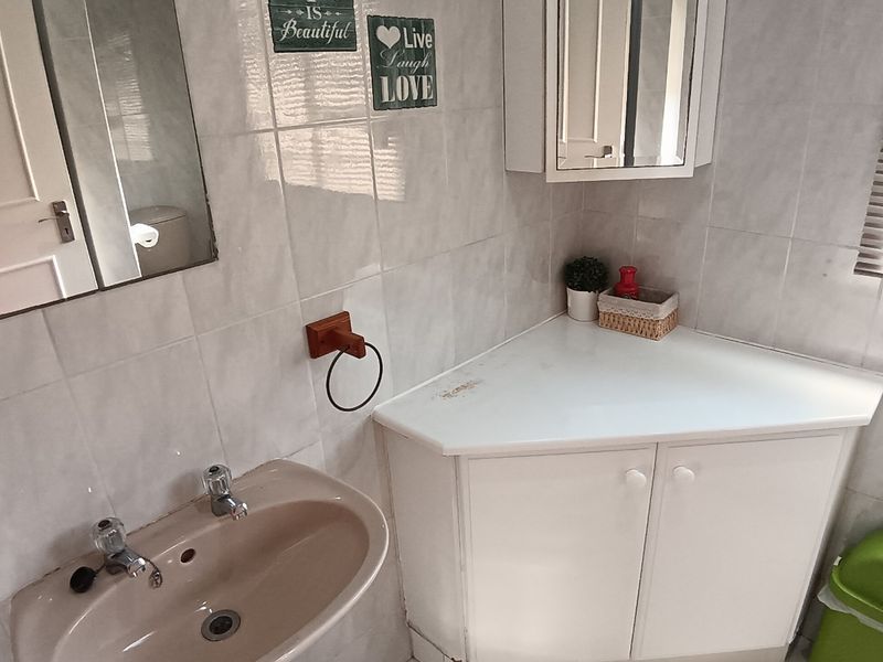 A functional bathroom featuring a pedestal basin, corner vanity unit with storage, and wall-mounted medicine cabinet, finished with neutral wall and floor tiling.
