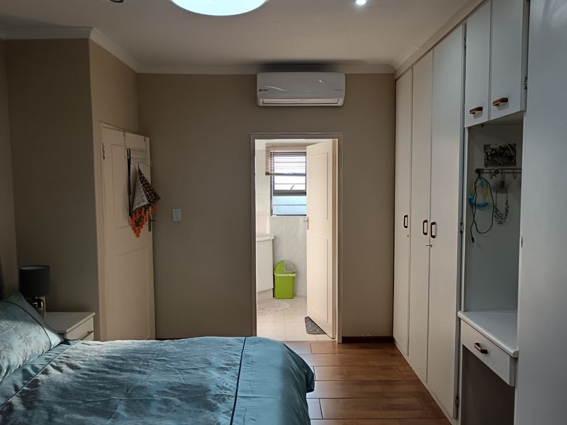 A well-maintained bedroom featuring built-in cupboards, laminate flooring, and an integrated air conditioning unit, with direct access to an en-suite bathroom.