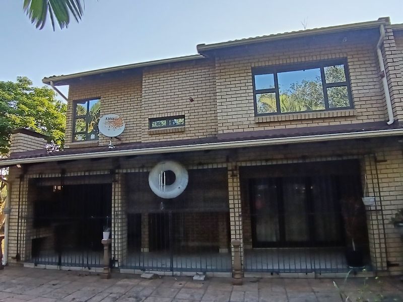 Rear view of a double-storey brick townhouse featuring a covered patio with built-in braai, security gates, and paved outdoor area.