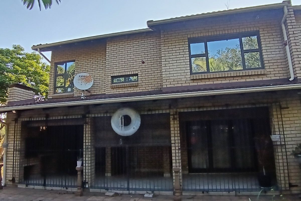 Rear view of a double-storey brick townhouse featuring a covered patio with built-in braai, security gates, and paved outdoor area.