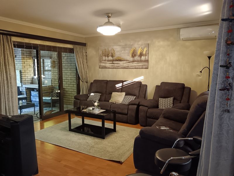 A comfortable living room featuring laminate flooring, a wall-mounted air conditioning unit, and large sliding glass doors that provide access to an outdoor patio area.