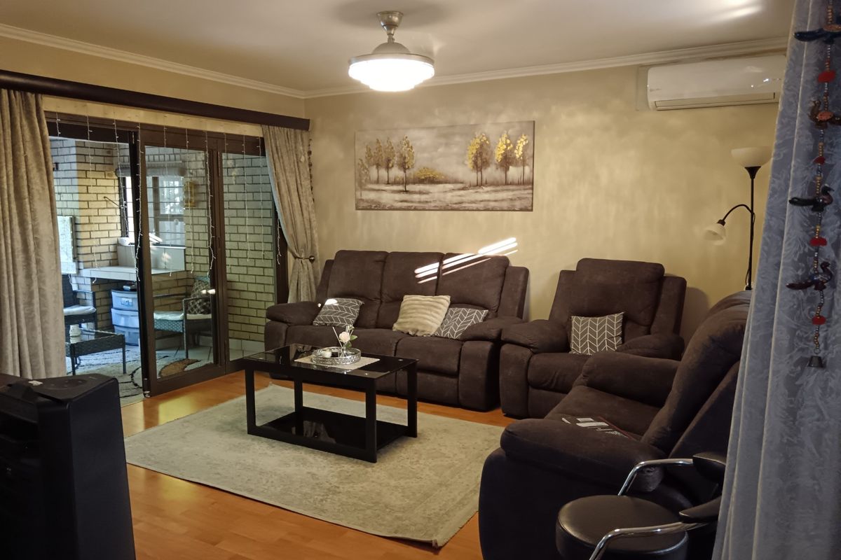 A comfortable living room featuring laminate flooring, a wall-mounted air conditioning unit, and large sliding glass doors that provide access to an outdoor patio area.