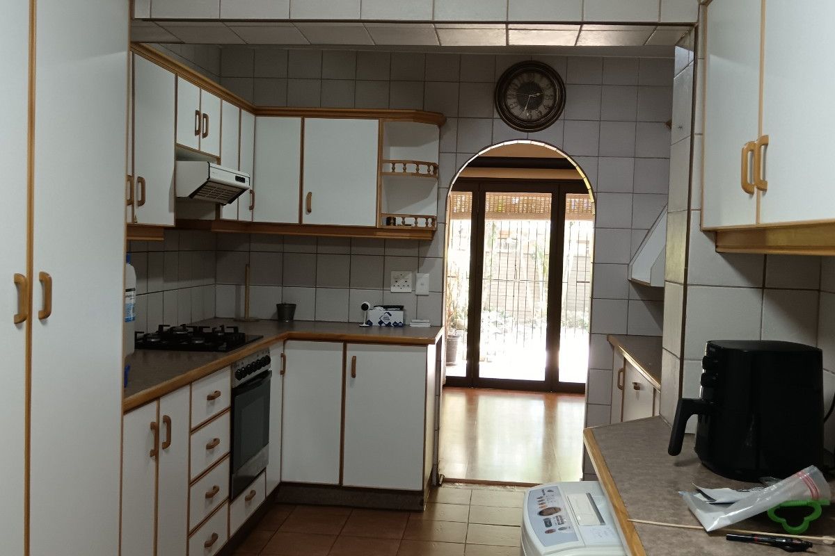 A functional kitchen featuring white cabinetry with wood trim, tiled backsplash, built-in oven and hob, leading through an archway to an adjacent living area.