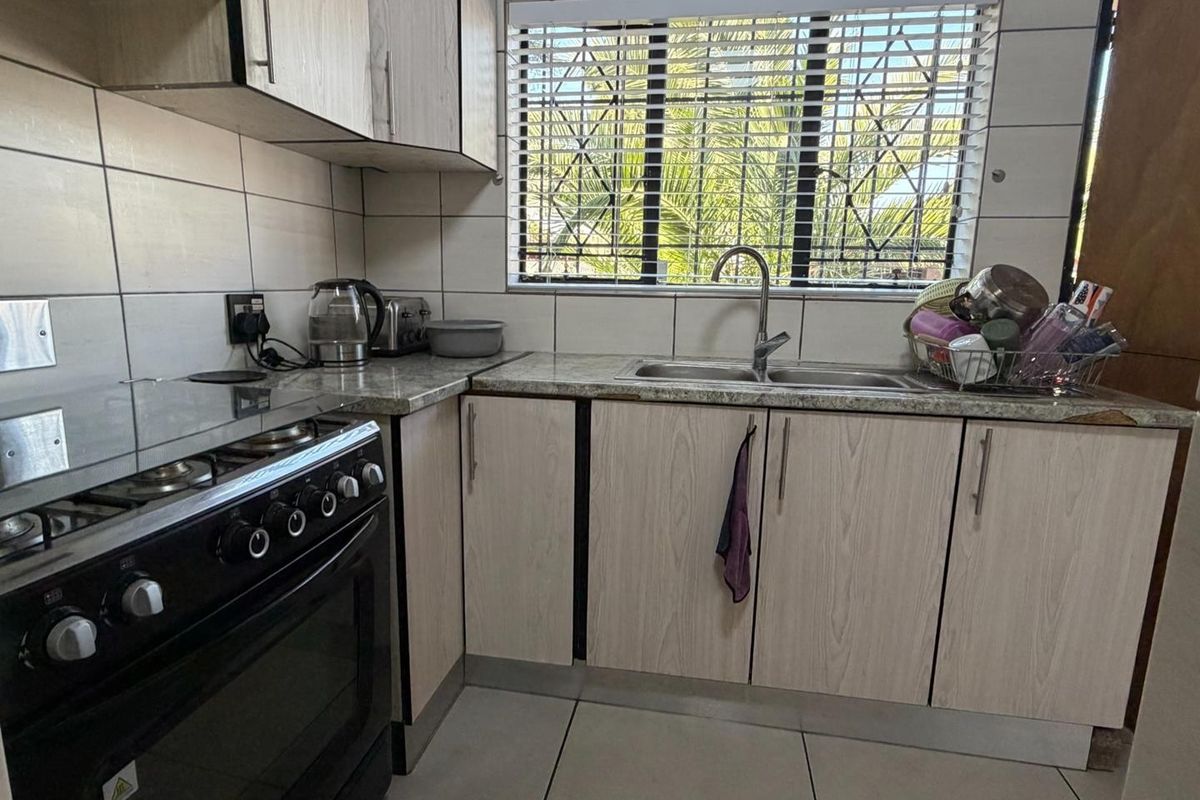 A functional kitchen featuring light wood-grain cabinetry, laminate countertops, a double basin sink, and a built-in gas stove with oven.