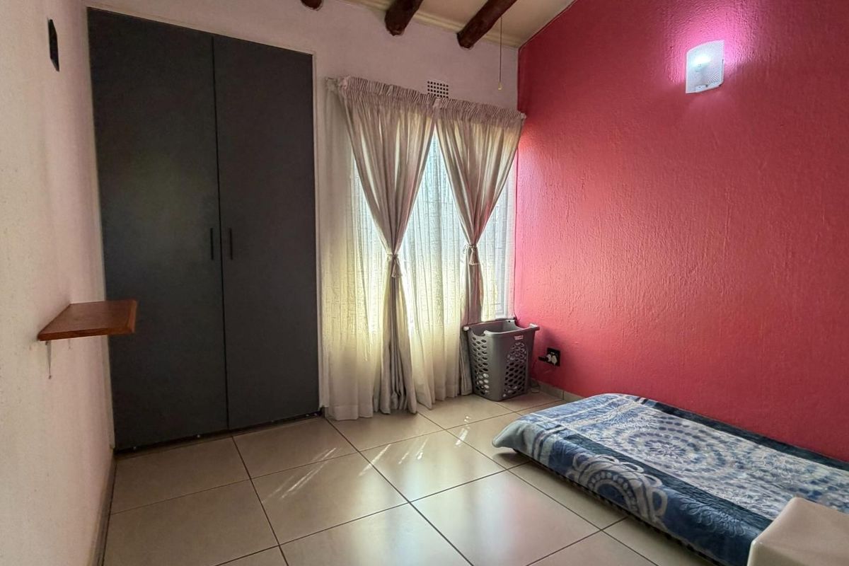 A bedroom featuring tiled flooring, exposed timber ceiling beams, and a built-in wardrobe, with a bold pink accent wall.