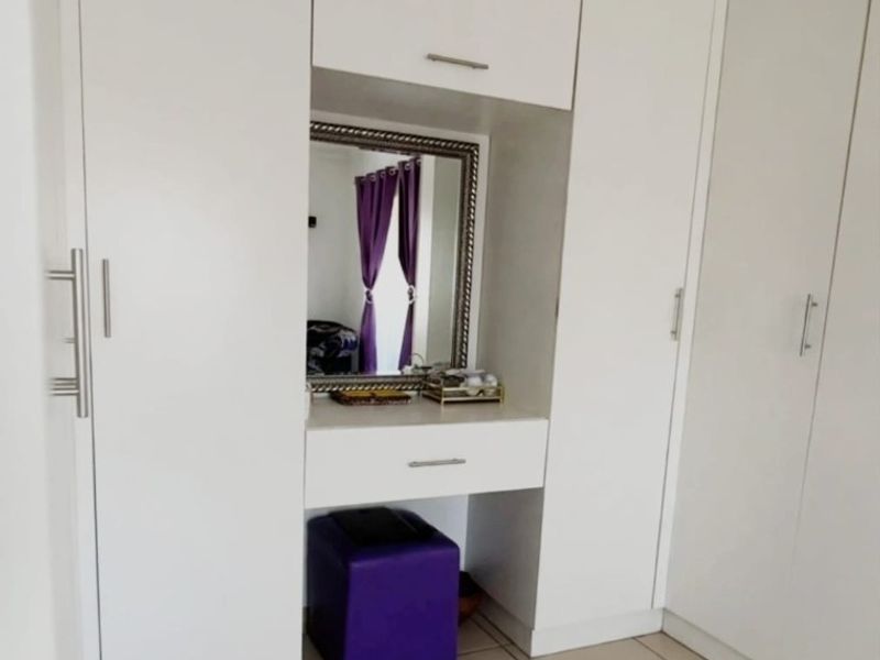 A well-maintained bedroom featuring white built-in cupboards with an integrated vanity station and neutral tiled flooring.