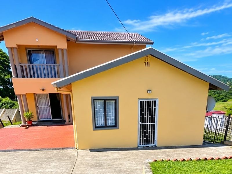 A two-story residential house featuring a yellow facade, a concrete driveway, a balcony, and secure entrance points.
