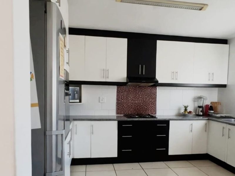 A functional kitchen featuring contrasting black and white cabinetry, a mosaic tile backsplash, gas hob with extractor, and neutral tiled flooring.