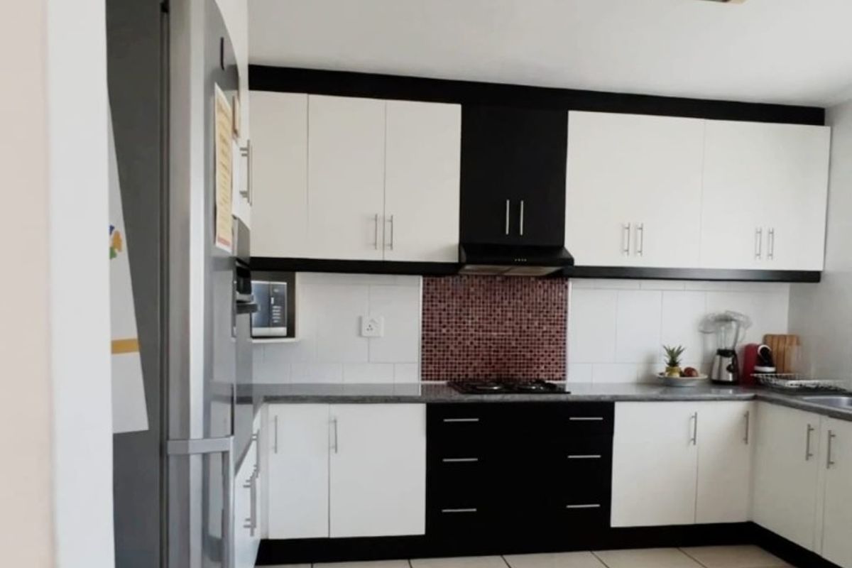 A functional kitchen featuring contrasting black and white cabinetry, a mosaic tile backsplash, gas hob with extractor, and neutral tiled flooring.