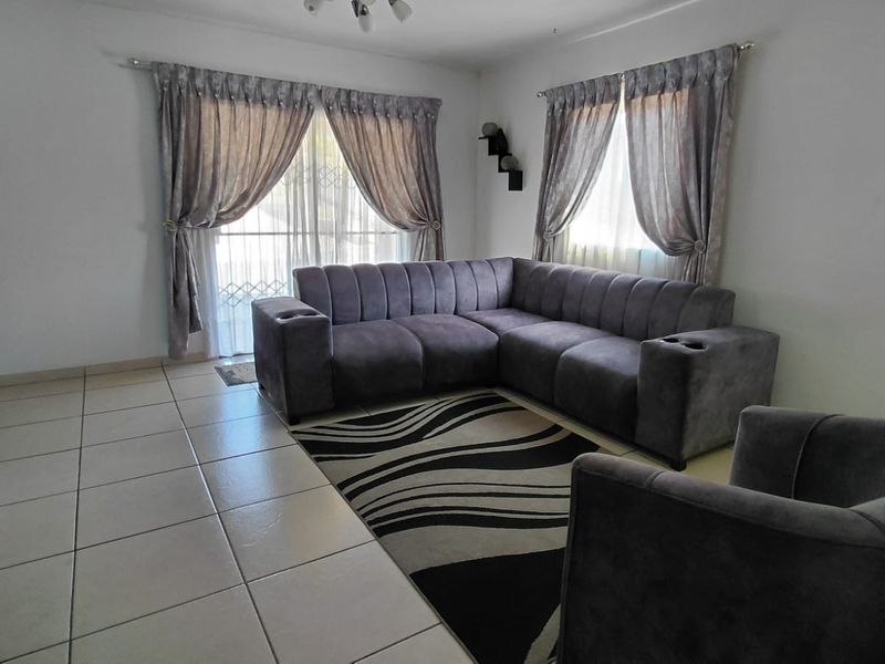 A bright living room featuring neutral tiled flooring and a sliding glass door with security gate, providing access to the exterior.