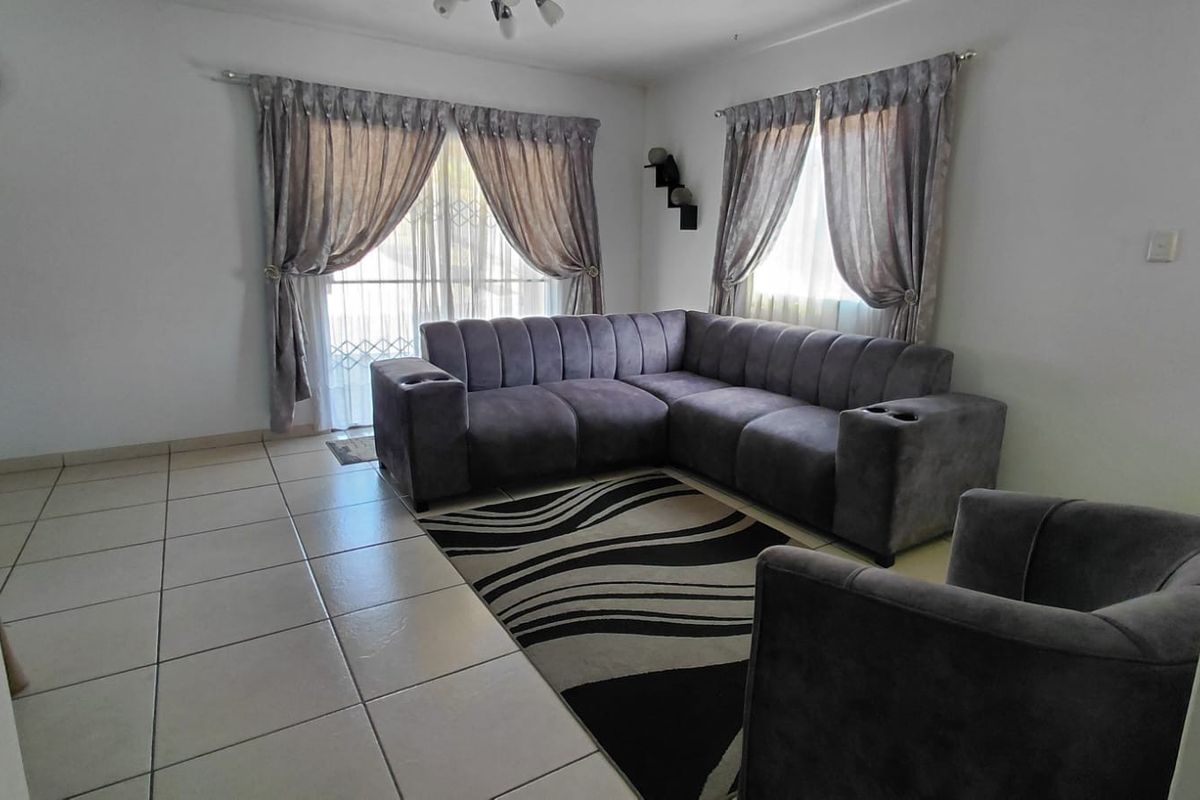 A bright living room featuring neutral tiled flooring and a sliding glass door with security gate, providing access to the exterior.