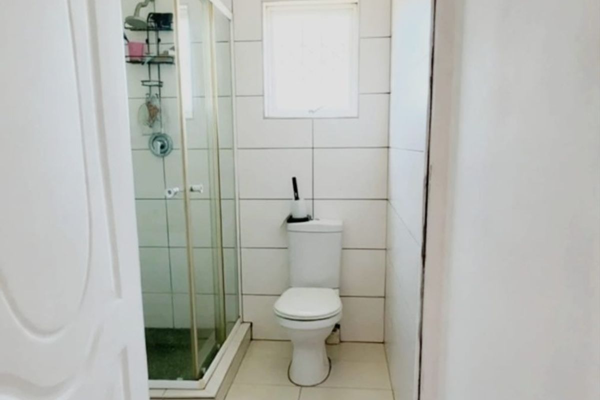 A functional bathroom featuring a shower enclosure, toilet, and neutral tiled finishes throughout.