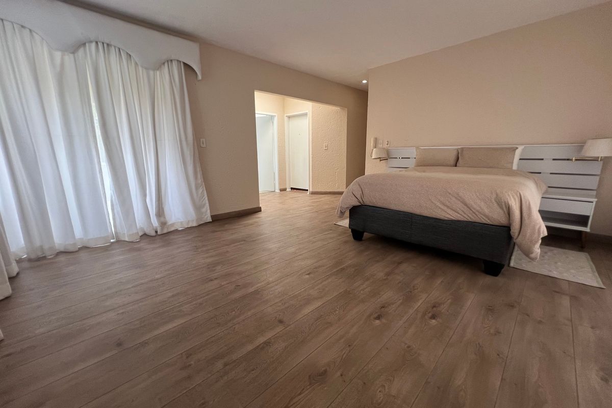 Spacious bedroom featuring modern laminate flooring, a built-in headboard, and access to an adjoining hallway.
