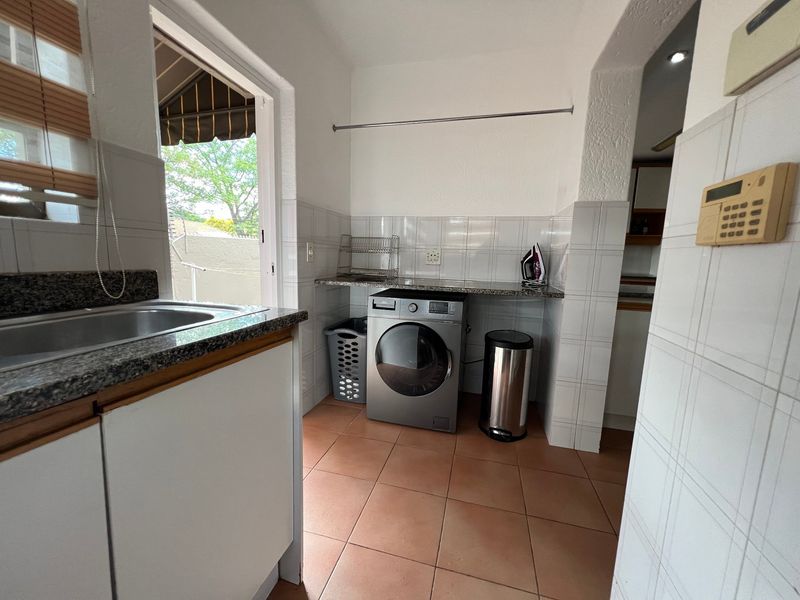 Functional laundry area featuring granite countertops, stainless steel sink, tiled finishes, and direct access to an outdoor space.