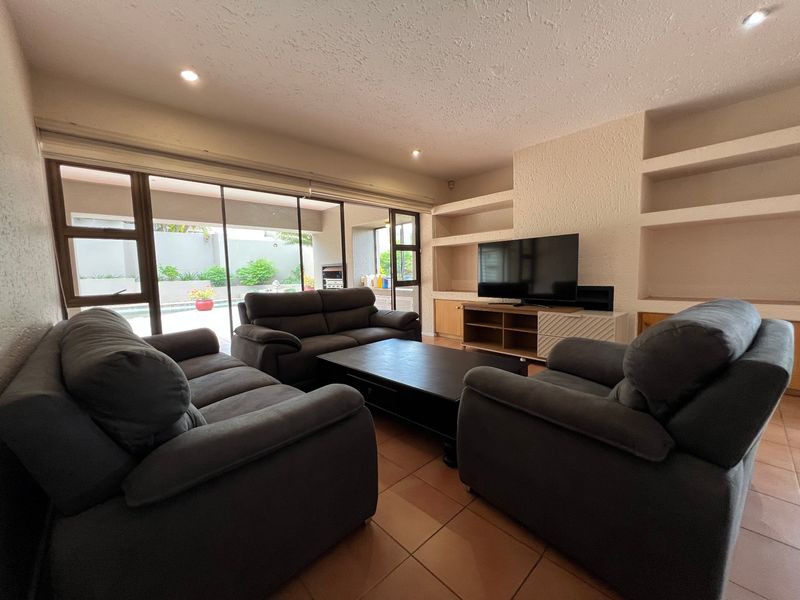 Spacious living room featuring built-in shelving, tiled flooring, and large sliding glass doors providing direct access to the outdoor patio and pool area.