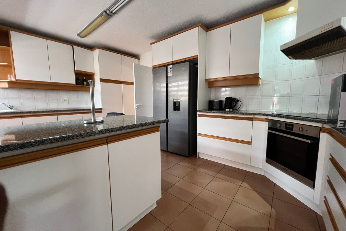 A functional kitchen featuring granite countertops, built-in cabinetry, a central island, and tiled flooring with integrated oven and extractor fan.