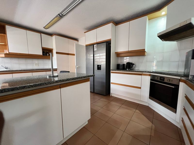 A functional kitchen featuring granite countertops, built-in cabinetry, a central island, and tiled flooring with integrated oven and extractor fan.