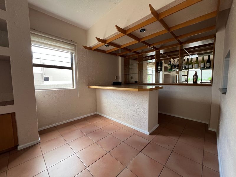 A dedicated bar area featuring a built-in counter, decorative wooden ceiling lattice, mirrored back bar, and tiled flooring.