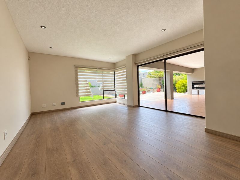 Spacious, light-filled living area featuring modern laminate flooring, recessed lighting, and large sliding glass doors that open onto a covered patio.