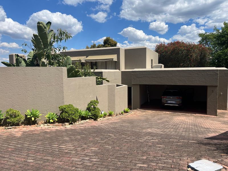 Front elevation of a modern house featuring a paved driveway, integrated double garage, and structured boundary walls with established landscaping.