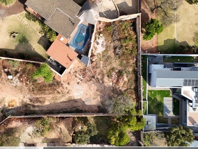 Aerial view of a residential vacant land plot situated between existing properties, featuring boundary walls and proximity to established homes.