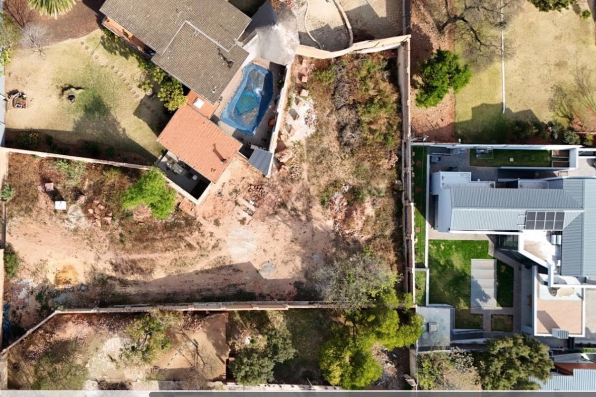 Aerial view of a residential vacant land plot situated between existing properties, featuring boundary walls and proximity to established homes.