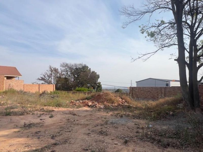 A vacant residential plot featuring brick boundary walls, mature trees, and some site debris, offering a blank canvas for future development.