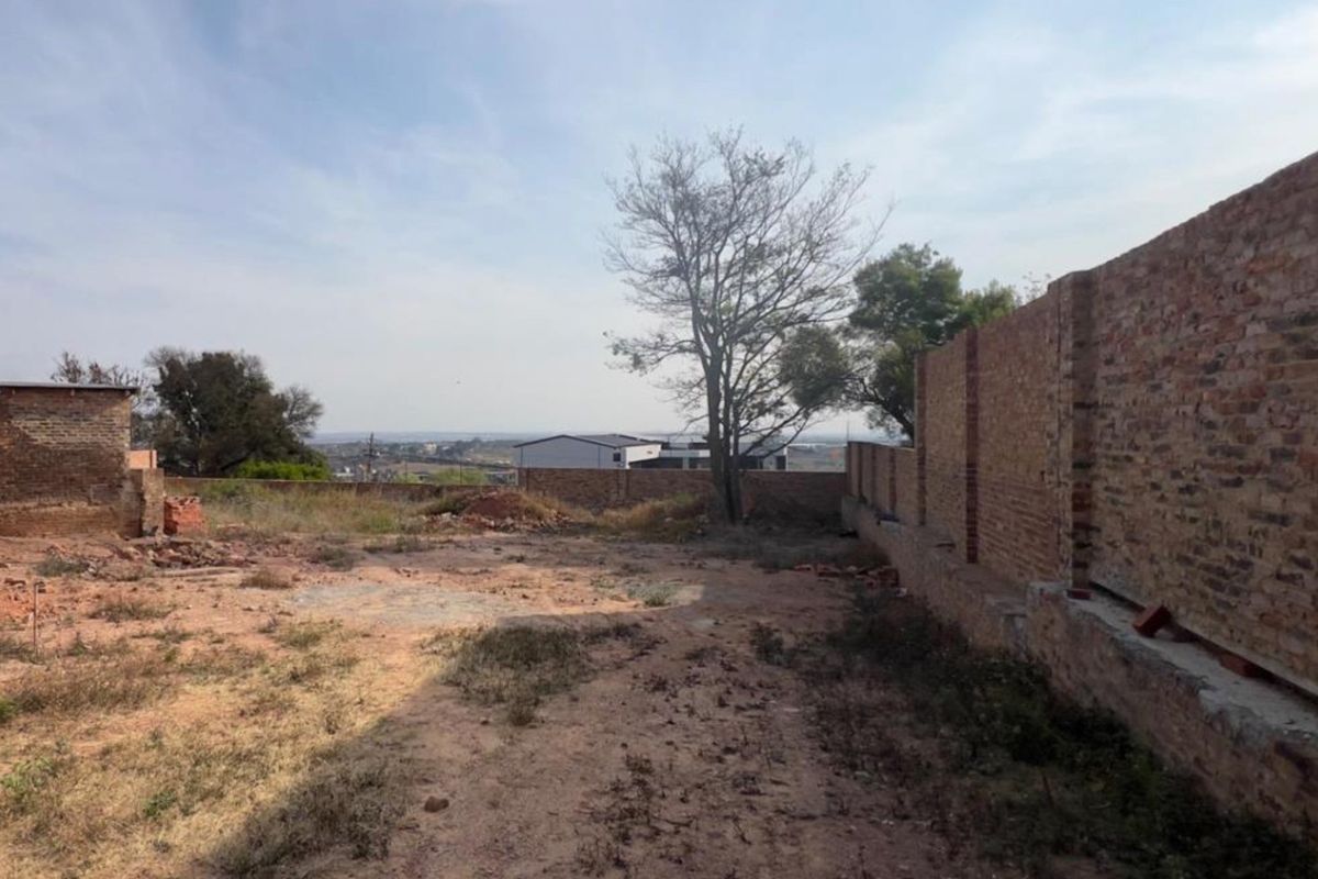 A vacant residential plot featuring a brick boundary wall and open land, offering potential for future development.