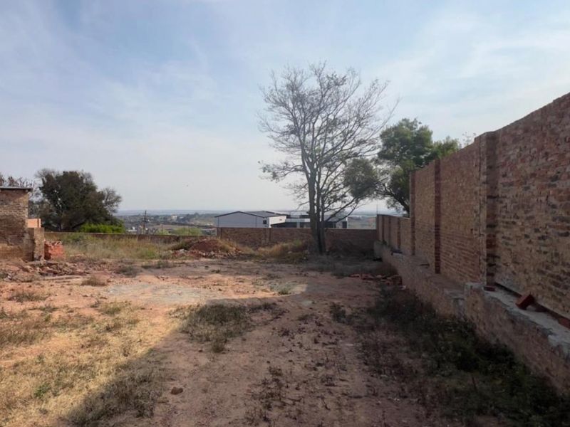 A vacant residential plot featuring a brick boundary wall and open land, offering potential for future development.