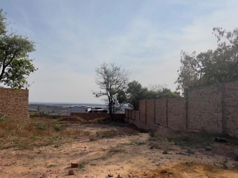 A vacant residential plot featuring established trees and brick boundary walls, offering a clear view of the surrounding landscape.