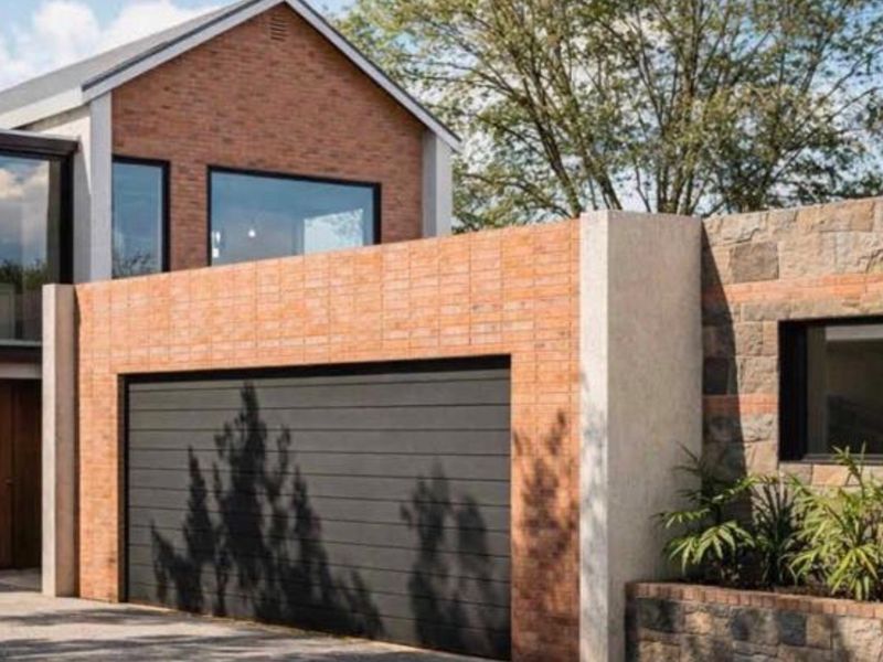 Modern residential facade featuring a combination of brick and stone cladding, a sleek sectional garage door, and integrated landscaping elements.