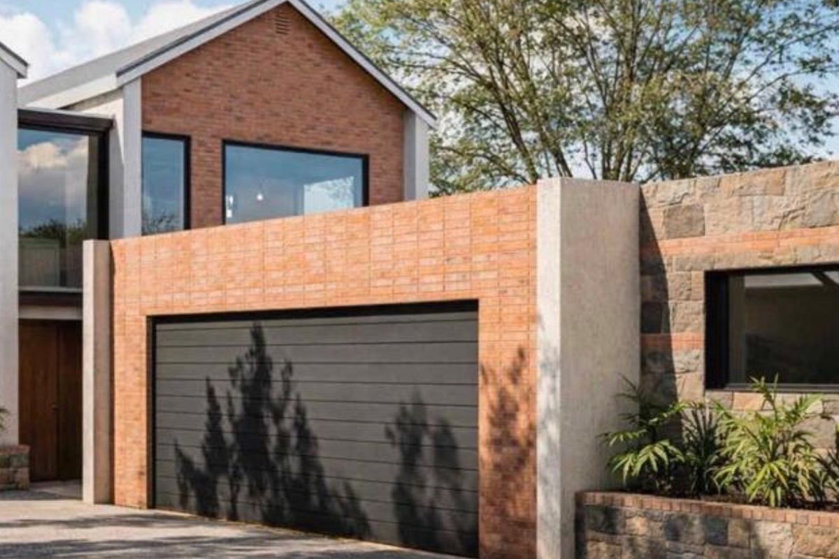 Modern residential facade featuring a combination of brick and stone cladding, a sleek sectional garage door, and integrated landscaping elements.