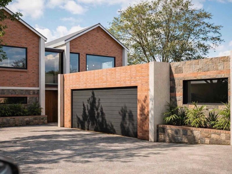 Modern residential facade featuring a combination of brick and stone cladding, an integrated garage, and a paved driveway entrance.