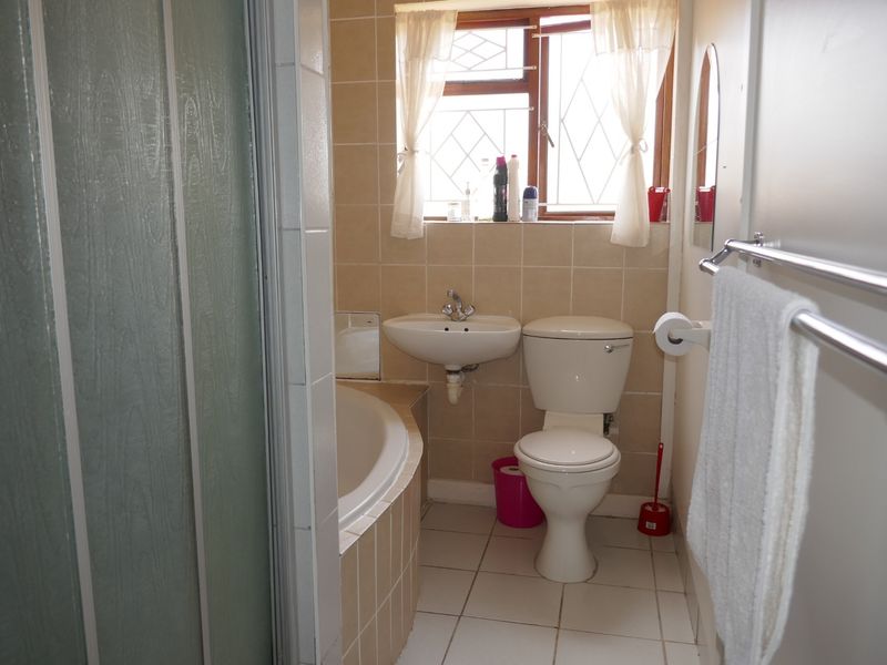 Compact bathroom featuring a built-in bathtub, wall-mounted basin, toilet, and neutral wall tiling with a security-grille window.