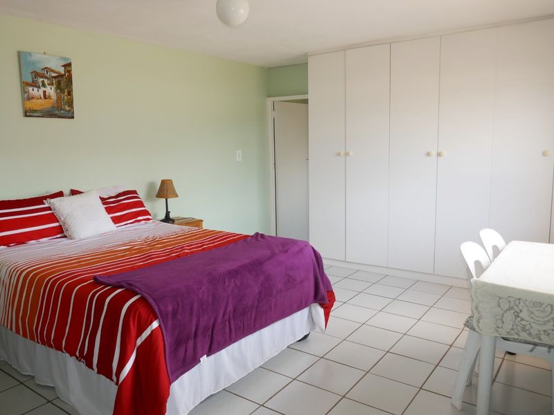 A spacious bedroom featuring neutral wall tones, white tiled flooring, and extensive built-in cupboard storage.