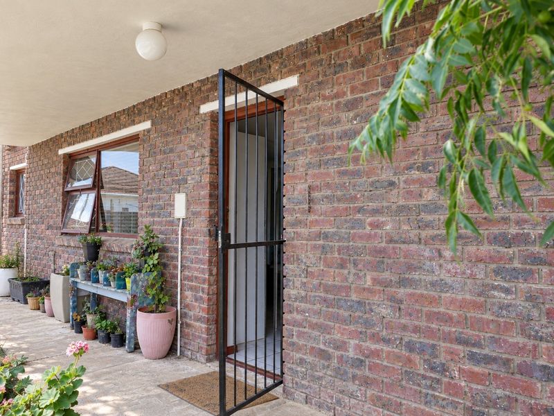 A covered brick patio area featuring a security gate entrance and casement windows, providing a functional outdoor space for the cottage.
