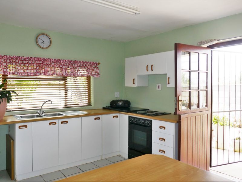 A functional kitchen featuring white cabinetry, a built-in oven and hob, stainless steel sink, and direct access to the outdoor area via a timber door.