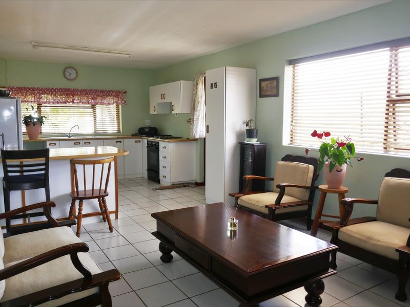 Open-plan living and kitchen area featuring tiled flooring, functional cabinetry, and large windows with venetian blinds, offering a practical and versatile living space.