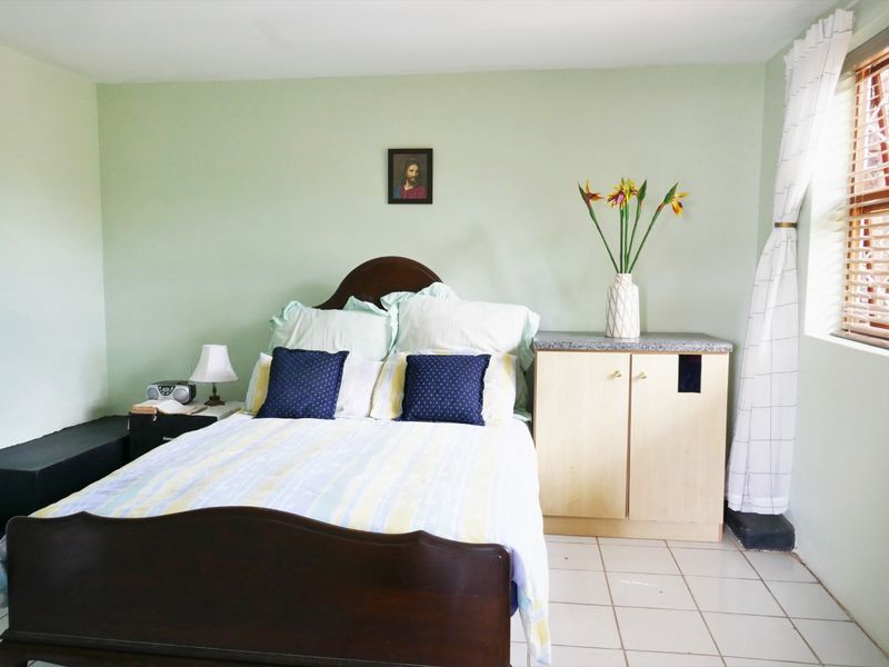 A bedroom featuring light green walls, tiled flooring, and a window with venetian blinds.