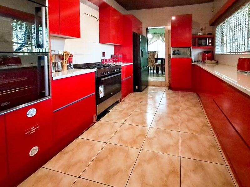A kitchen featuring vibrant red cabinetry, tiled flooring, and built-in appliances, offering a functional layout with potential for cosmetic updates.