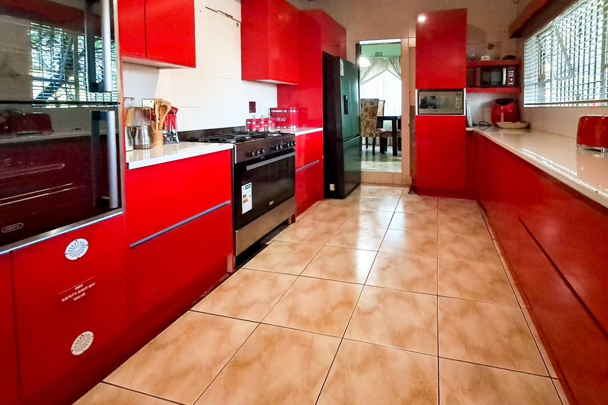 A kitchen featuring vibrant red cabinetry, tiled flooring, and built-in appliances, offering a functional layout with potential for cosmetic updates.