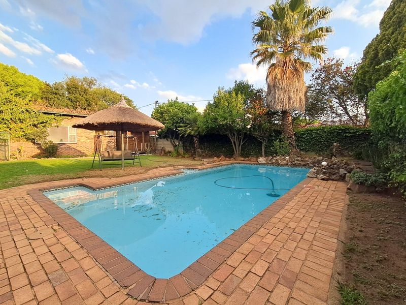 Outdoor pool area featuring a swimming pool with brick paving, a rockery feature, and a surrounding garden with a lawn and perimeter wall.