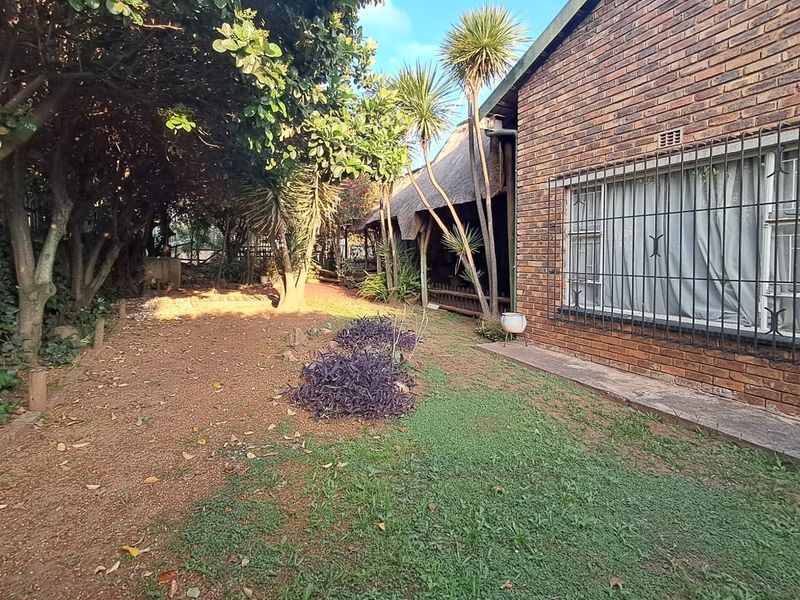 Rear garden area featuring a face brick exterior, thatched roof section, and security-barred windows, set within a mature landscaped yard.