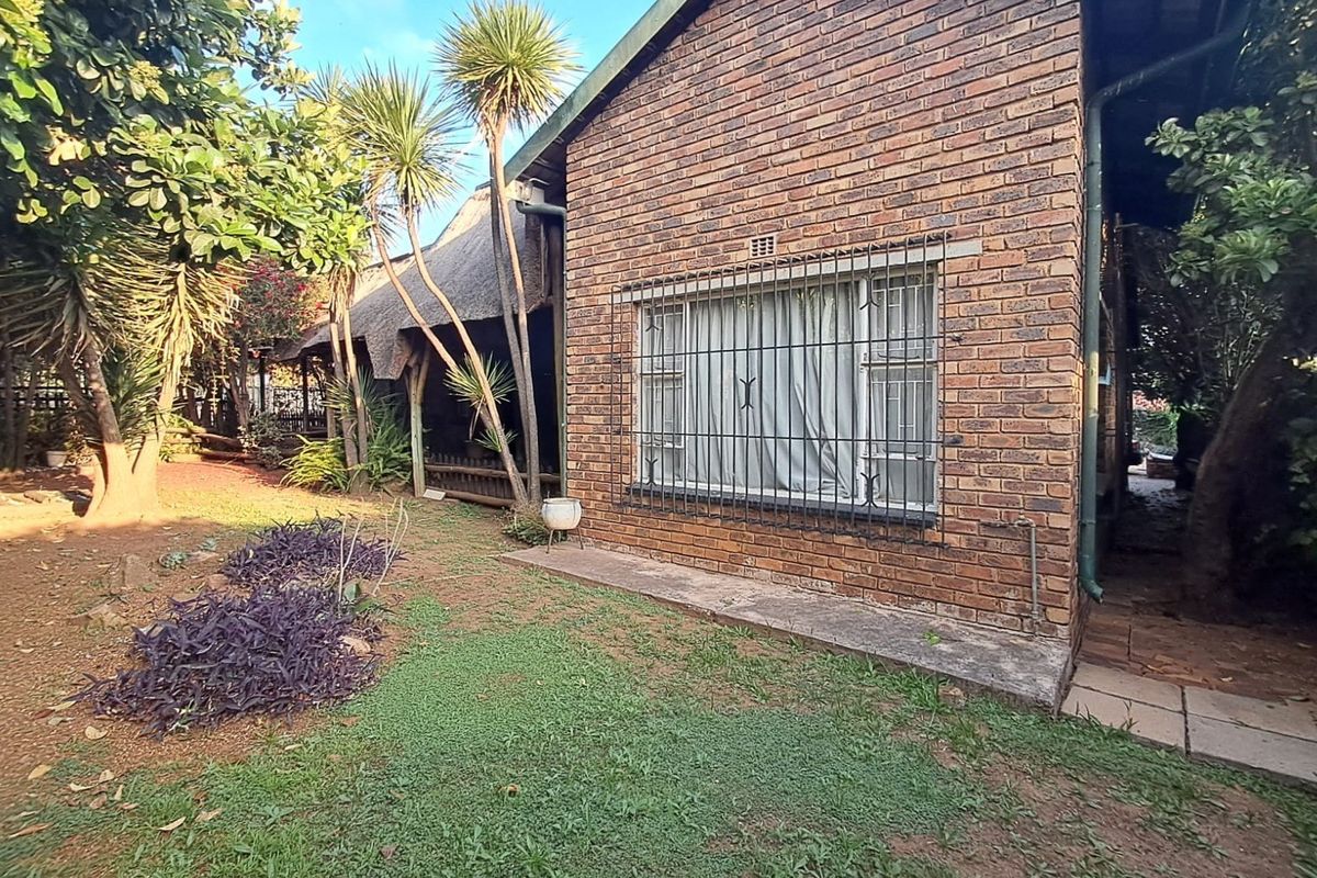 Rear view of the property featuring a face brick facade, security bars on windows, and a thatched roof section overlooking the garden area.
